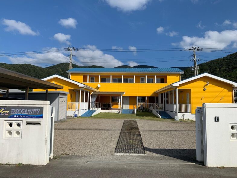 ゼログラビティせいすいヴィラの外観は、鮮やかな黄色の外壁が特徴です。施設前には駐車場があります。